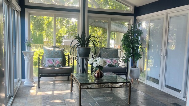 A sunlit room with a glass coffee table, a ceiling fan, and a view of greenery outside. - Peaceful Lakeside Escape• Trails & Parks Nearby (Grimsby)