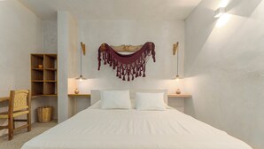 A neatly made bed with a white sheet, two pillows, and a hanging macrame piece above it. There are two bedside tables with lamps, a wooden chair, and a wicker basket on the floor. - Luxury Oceanfront Double Villa With Pool (Puerto Escondido)