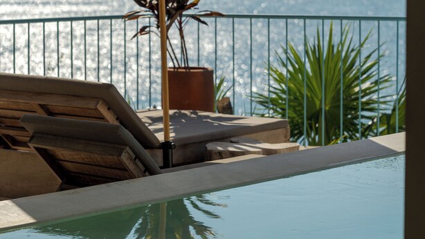 An infinity pool with lounge chairs and a potted plant, overlooking a body of water. - Luxury Oceanfront Double Villa With Pool (Puerto Escondido)