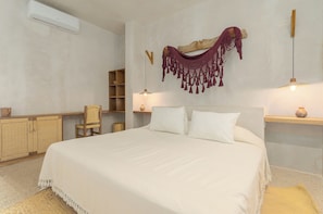 Un dormitorio con una cama grande, un armario de madera, una silla y un adorno colgante de macramé.