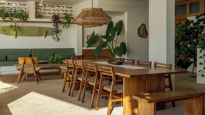 A dining area with a wooden table and chairs, surrounded by green plants and a green sofa. - Luxury Oceanfront Double Villa With Pool (Puerto Escondido)