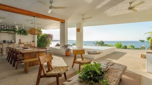 A spacious outdoor dining area with a view of the sea, wooden furniture, ceiling fans, and potted plants. - Luxury Oceanfront Double Villa With Pool (Puerto Escondido)