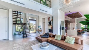 Uma sala de estar ampla com uma escada moderna, um sofá seccional marrom grande e um lustre contemporâneo.