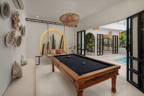 Ein Billardtisch in einem modernen Raum mit einer Couch, Wandkunst und Blick ins Freie.