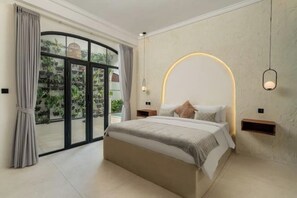 Ein modernes Schlafzimmer mit einem großen Bett, einer Wandlampe mit gebogenem Arm und Blick durch eine Glastür.
