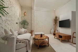 Ein modernes Wohnzimmer mit strukturierter Wand, einer Couch, einem runden Holztisch, einem an der Wand befestigten Fernseher und einem Nachttisch aus Holz.