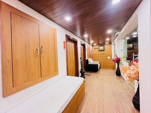 A hallway with wooden cabinets, a bed, a sofa, and a vase with flowers. - Hotel Gulmarg Residency (Mount Abu)