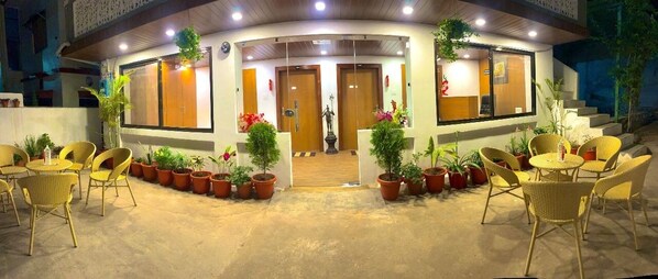 A hotel entrance with a curved facade, potted plants, wicker chairs, and a statue in the center. - Hotel Gulmarg Residency (Mount Abu)