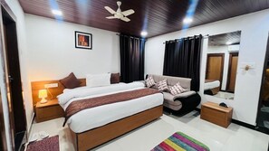 A bedroom with a bed, nightstands, a dresser, a mirror, and a ceiling fan. - Hotel Gulmarg Residency (Mount Abu)