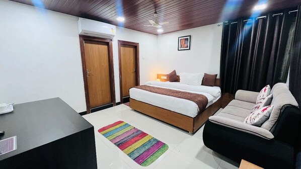 A bedroom with a bed, a sofa, a desk, and a colorful rug. - Hotel Gulmarg Residency (Mount Abu)