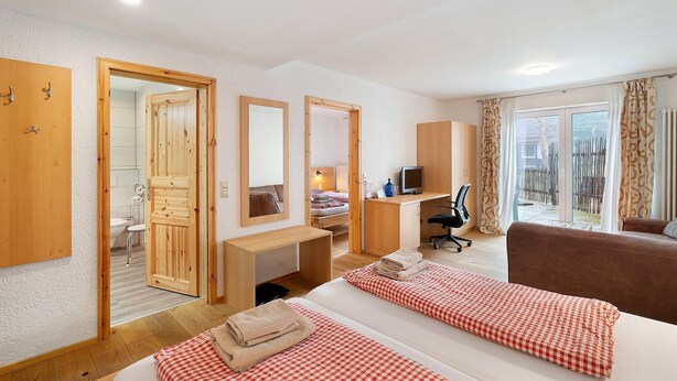 Ein Hotelzimmer mit zwei Betten, einem Schreibtisch, einem Sessel, einem Fernseher und Blick ins Freie.