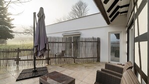 Eine Terrasse mit Korbmöbeln, einem Steintisch und einem Holzzaun.
