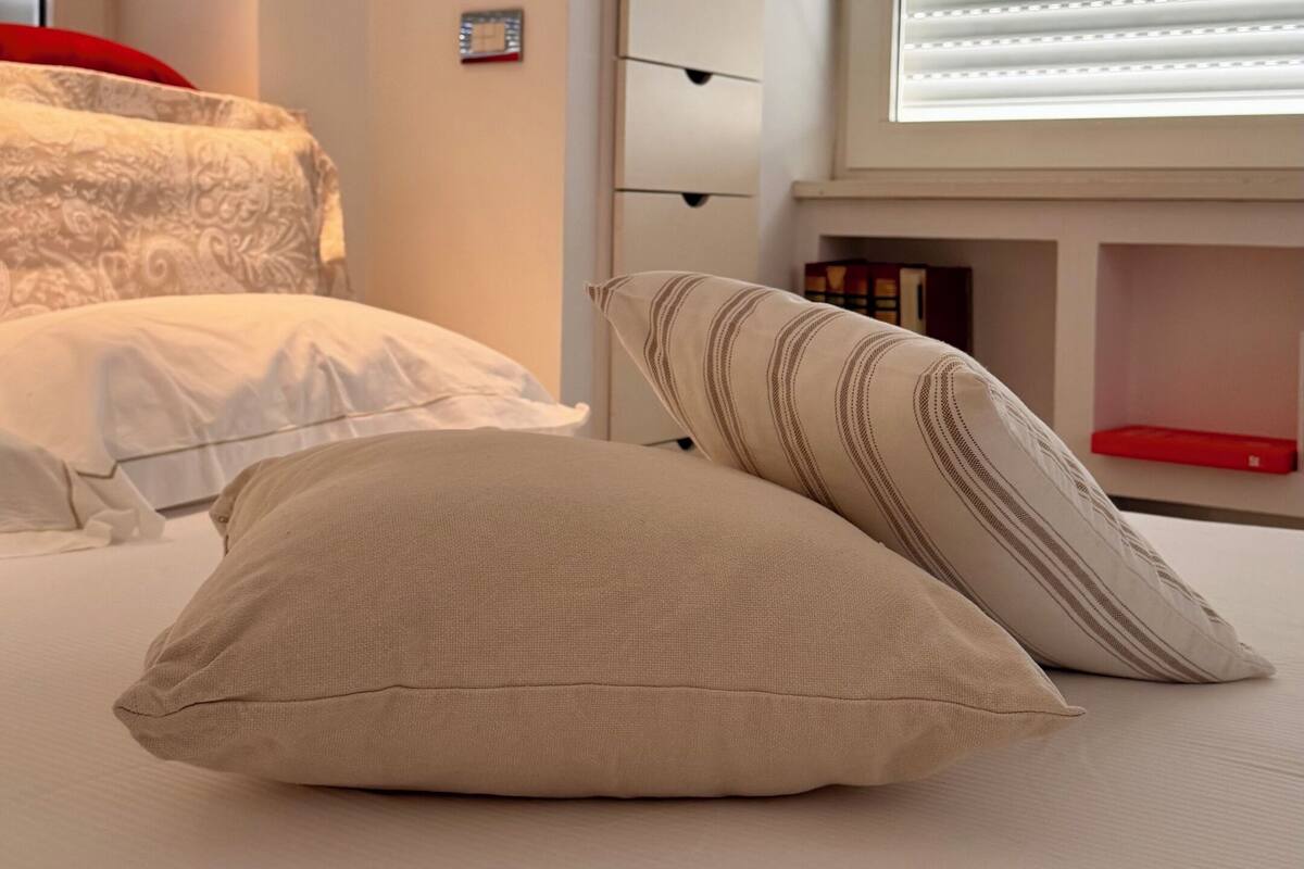 Ein Schlafzimmer mit Bett, Kissen, einem Schminktisch und einem Fenster mit Jalousien.