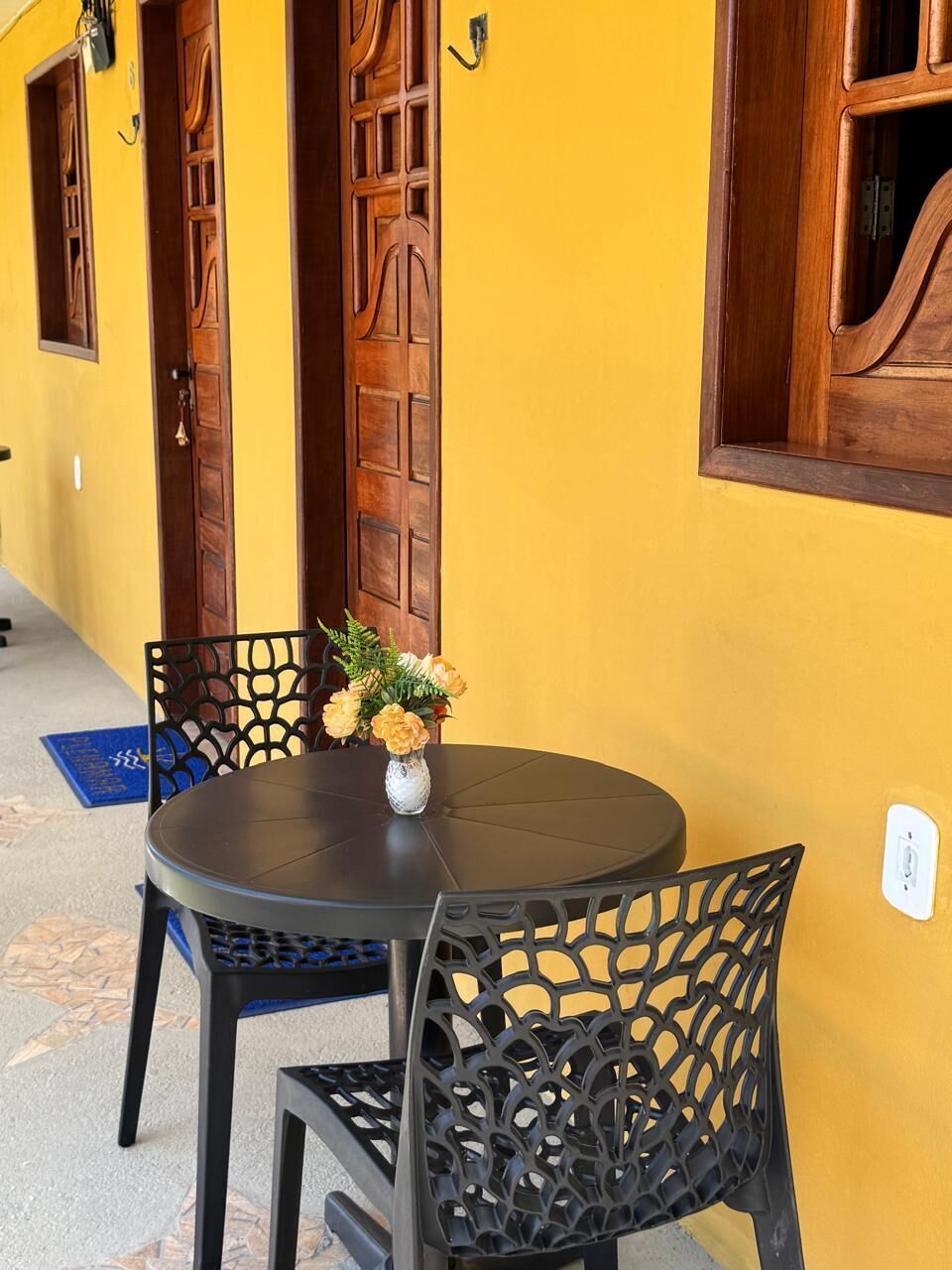 Una mesa redonda con sillas, un jarrón con flores y puertas de madera frente a una pared amarilla.