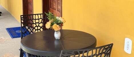 A round table with chairs, a vase with flowers, and wooden doors against a yellow wall.