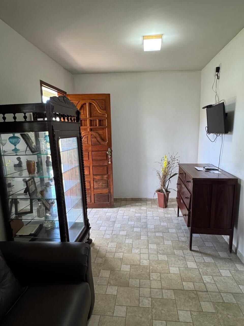 Una sala de estar con un aparador de vidrio, una puerta de madera, un televisor montado en la pared y un sofá de cuero marrón.