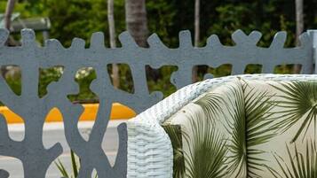 A wicker outdoor seating area with a white cushioned chair and a round table with books.