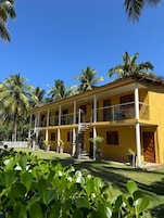 Um edifício amarelo de dois andares com uma varanda, cercado por palmeiras.