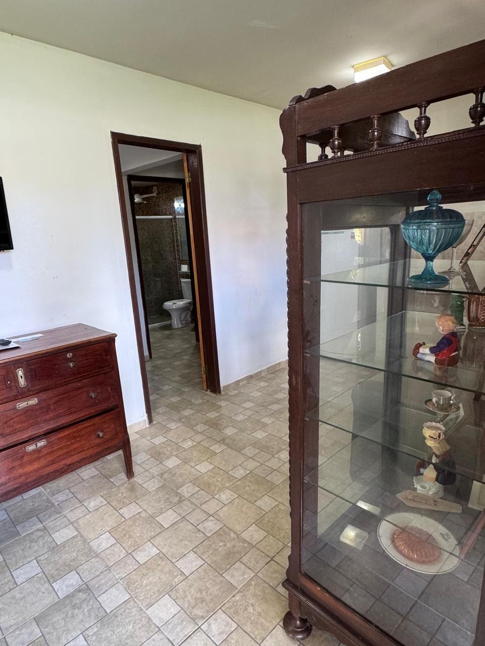A room with a wooden dresser, a glass-fronted cabinet, and a doorway leading to a bathroom.