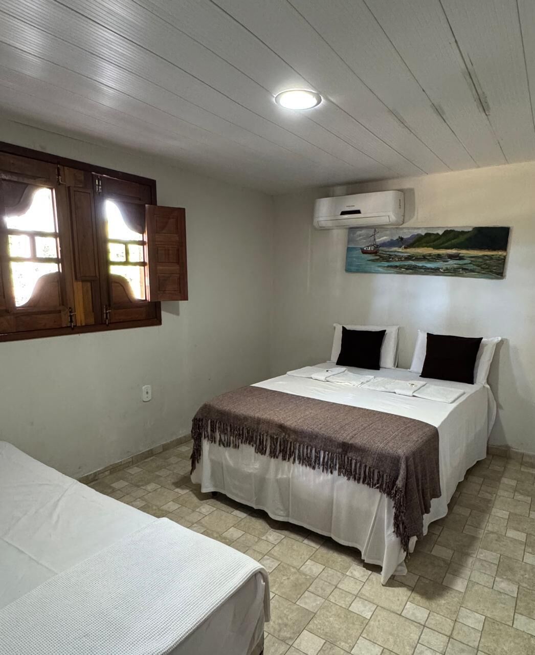 Een kamer met een bed, een raam met gordijnen, een airconditioning en een schilderij aan de muur.