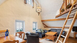 Un espacio tipo loft con una escalera de madera, un sofá, una mesa y una lámpara colgante.