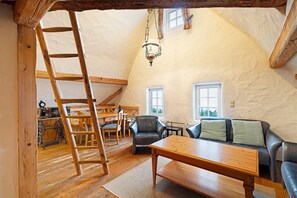 Ein Loft-Zimmer mit Holzleiter, einer Couch, einem Tisch und einer Chandelier.