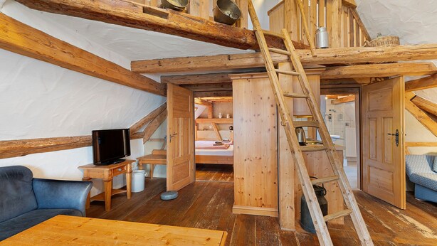 Habitación estilo loft con vigas de madera a la vista, una cama en altillo, televisión y una mesa de madera.