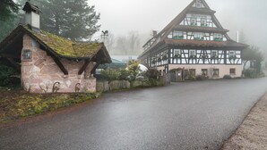 Un edificio tradicional de entramado de madera con chimenea de piedra y una pequeña construcción adyacente.