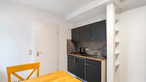 Une cuisine de taille réduite, avec des meubles de couleur sombre, une table en bois et une porte blanche.