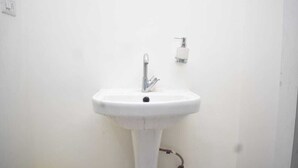 Un lavabo a colonna bianca con rubinetto ed erogatore di sapone montati a parete.