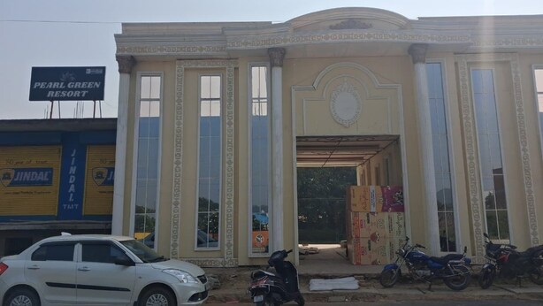 Un edificio con un grande cartello che indica 'Pearl Green Resort' e 'Jindal TMT'. Si vedono auto e motociclette parcheggiate davanti.