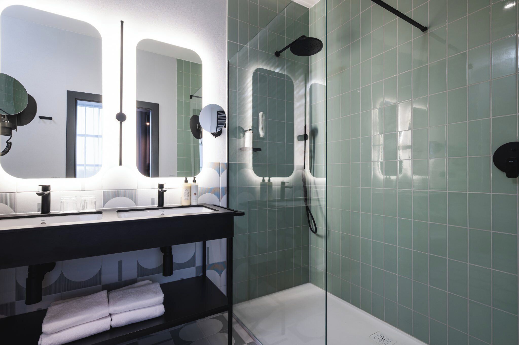 A modern bathroom with a glass-enclosed shower, a black vanity with a mirror, and a shelf with folded towels.