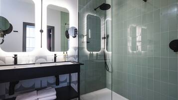 A modern bathroom with a glass-enclosed shower, a black vanity with a mirror, and a shelf with folded towels.
