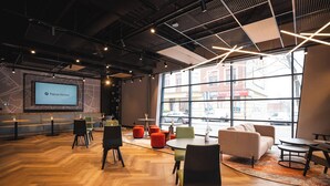 Un'accogliente hall d'hotel moderna con un grande schermo che mostra il nome dell'hotel, pavimento in legno e diverse opzioni di seduta, tra cui poltrone e divani.