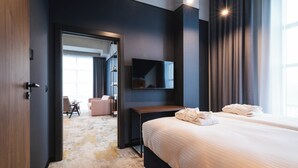 Una camera d'albergo moderna con un letto grande, una televisione a schermo piatto montata a parete e vista sull'interno della stanza attraverso una porta aperta.