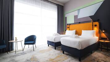 A hotel room with two beds, a small table, two chairs, and a large window with curtains.