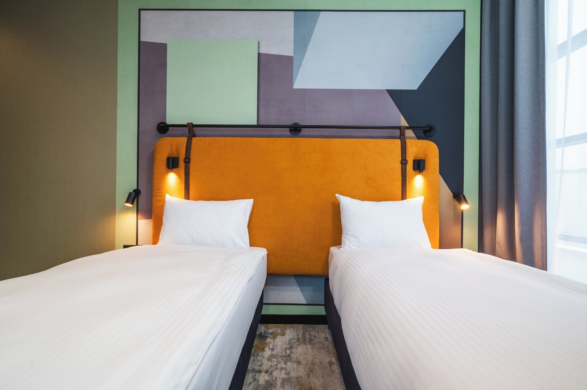 A hotel room with two single beds, a modern headboard, and a geometric wall design.
