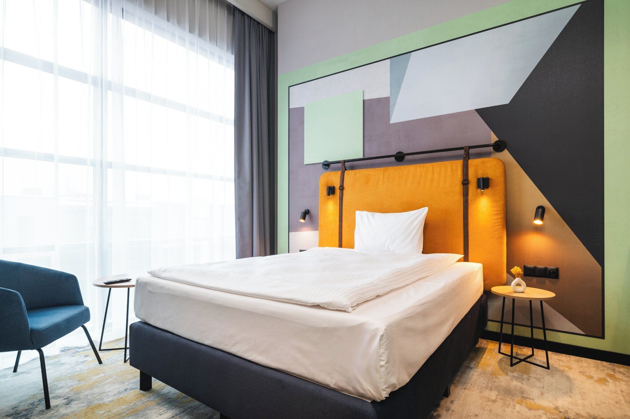 Une chambre d’hôtel moderne avec un grand lit, une petite table d’appoint, une chaise et une grande fenêtre avec des rideaux.