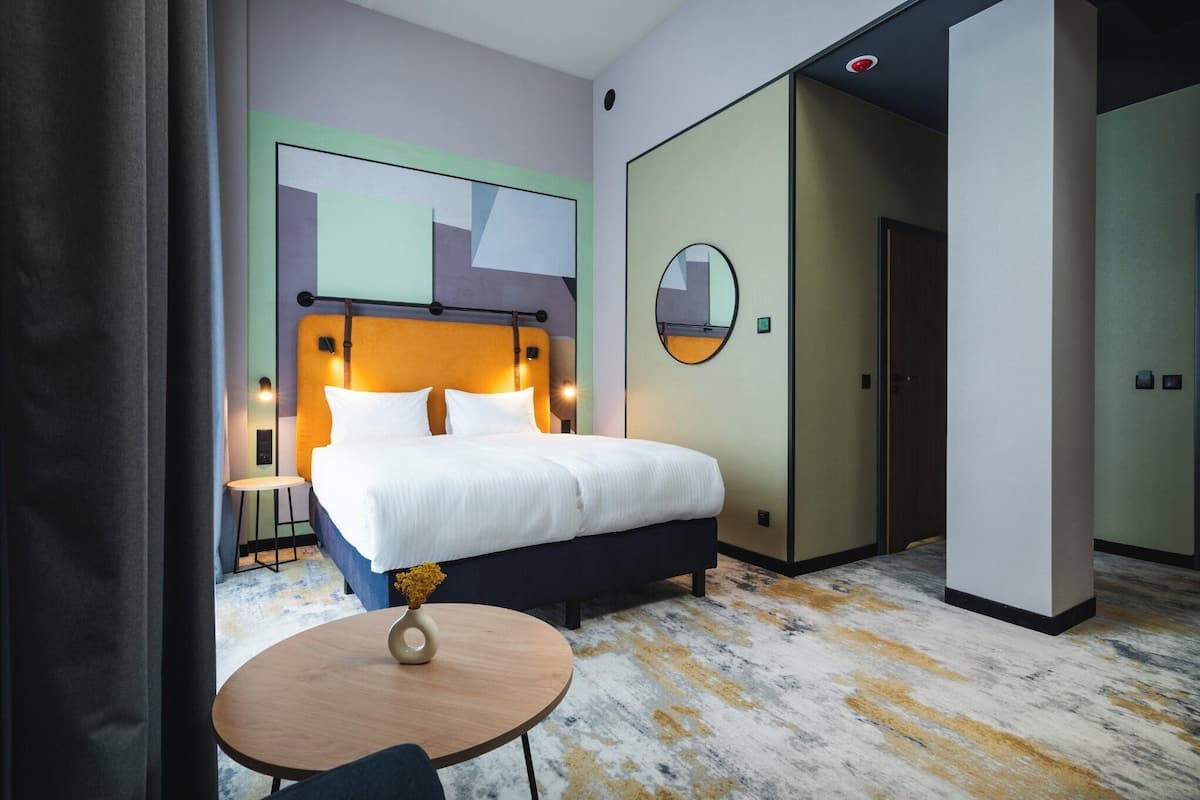 Una habitación de hotel con cama, mesita de noche y un espejo redondo en la pared.