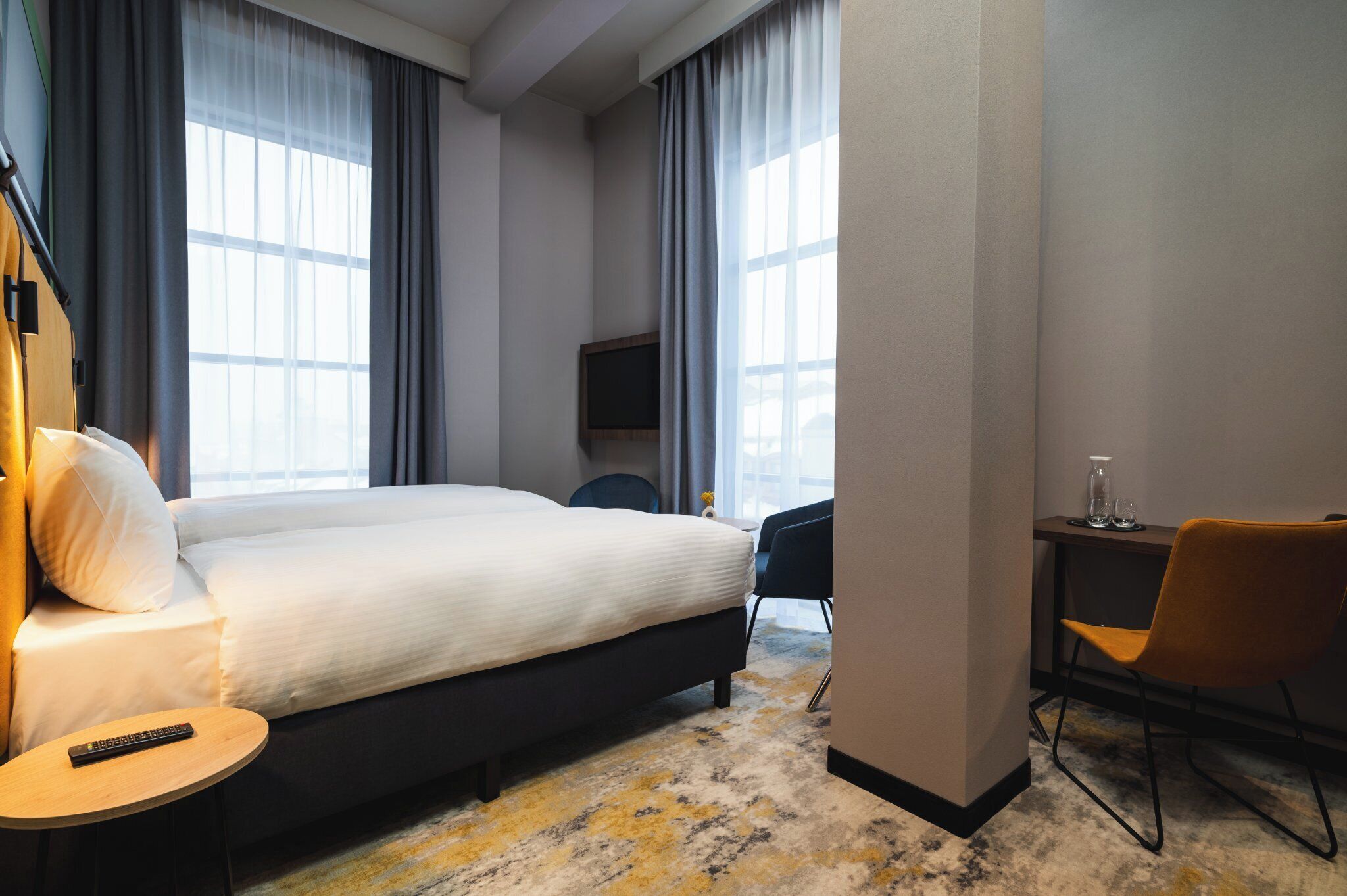 Una habitación de hotel con una cama grande, un escritorio con silla, televisor y ventana con cortinas.
