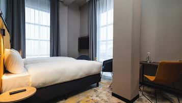 Una habitación de hotel con una cama grande, un escritorio con silla, televisor y ventana con cortinas.