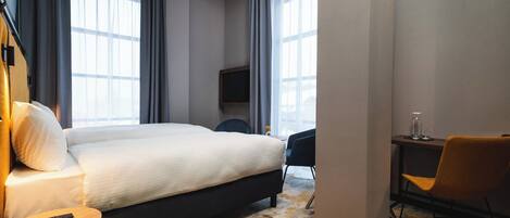 Una habitación de hotel con una cama grande, un escritorio con silla, televisor y ventana con cortinas.