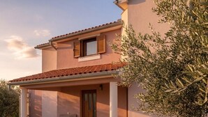 Una casa de dos pisos con un porche cubierto, mobiliario exterior y un jardín.