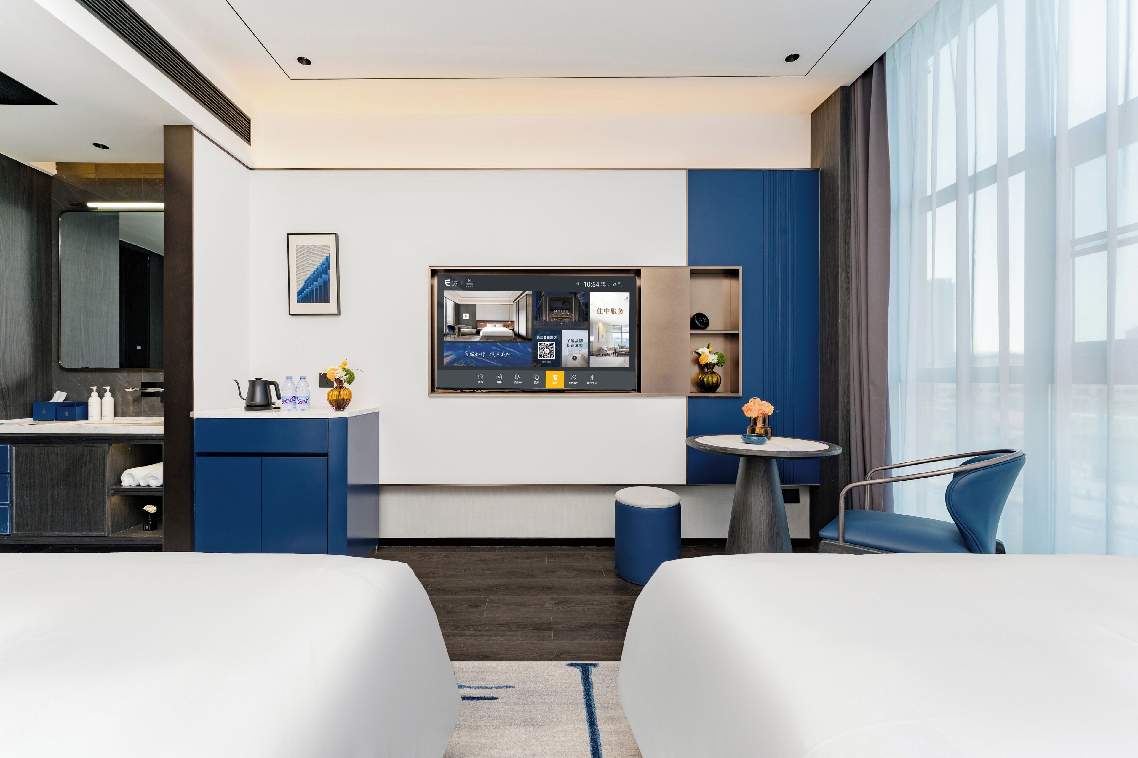 A modern hotel room with a bed, a desk, a chair, a small table, and a large window.