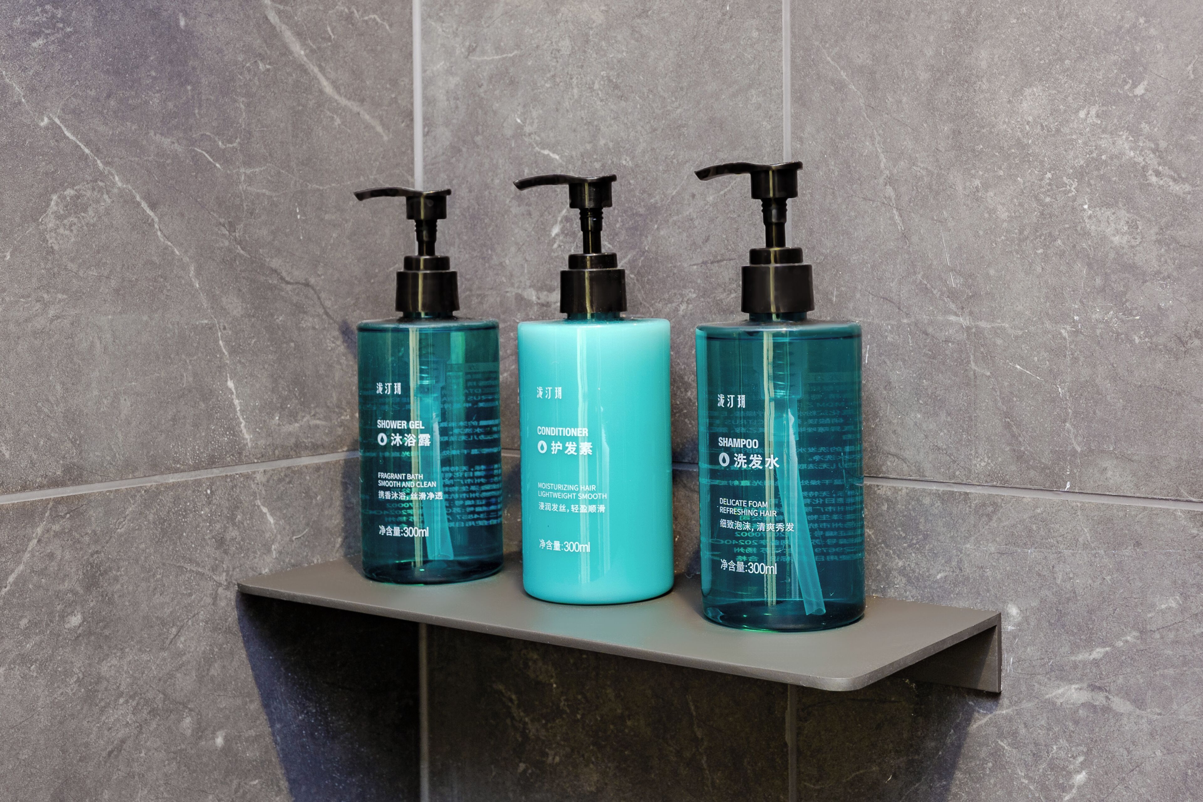 Three bottles of personal care products on a shelf against a tiled wall.