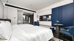 A modern hotel room with a large bed, a desk with a computer, a chair, and a small table with a vase.