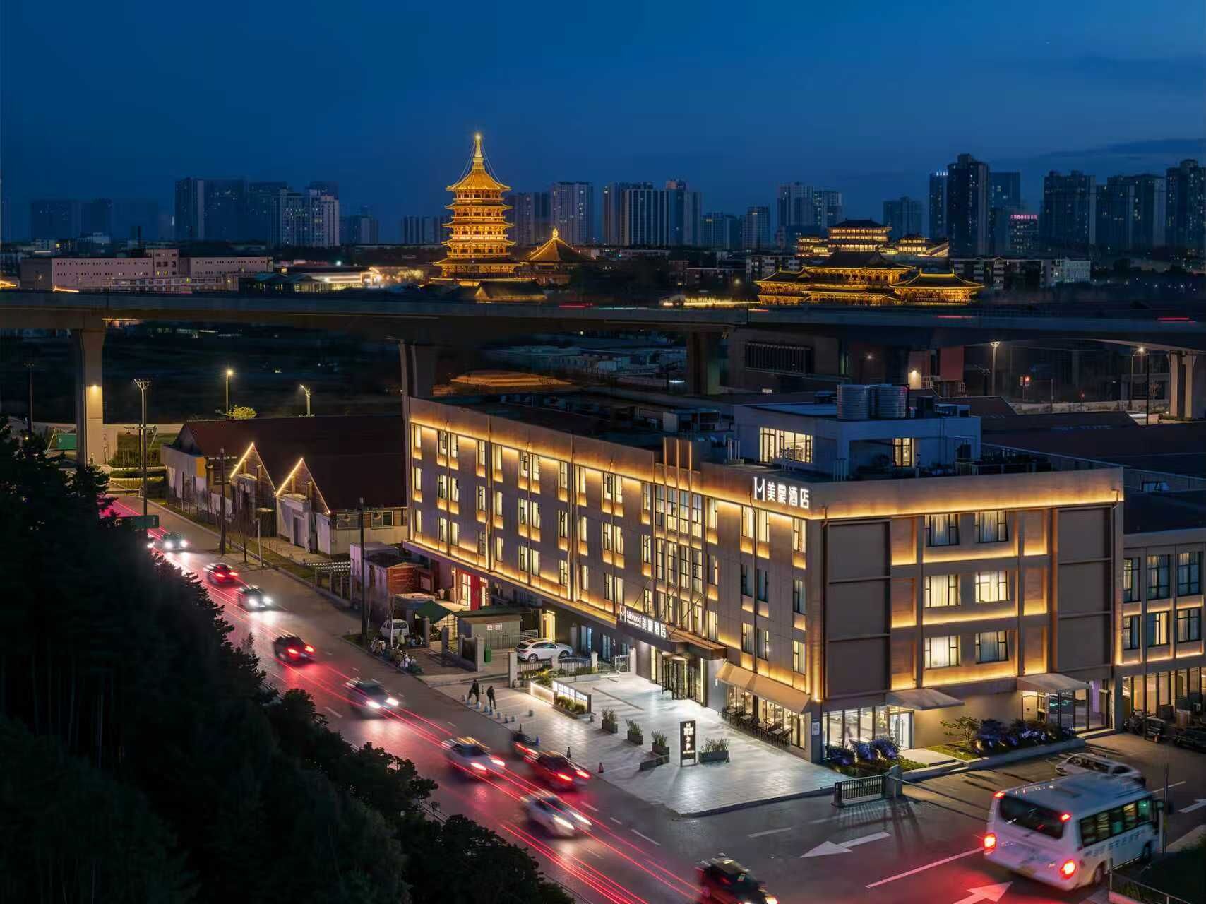 A hotel with a modern facade, a traditional pagoda in the background, and a busy street with vehicles.