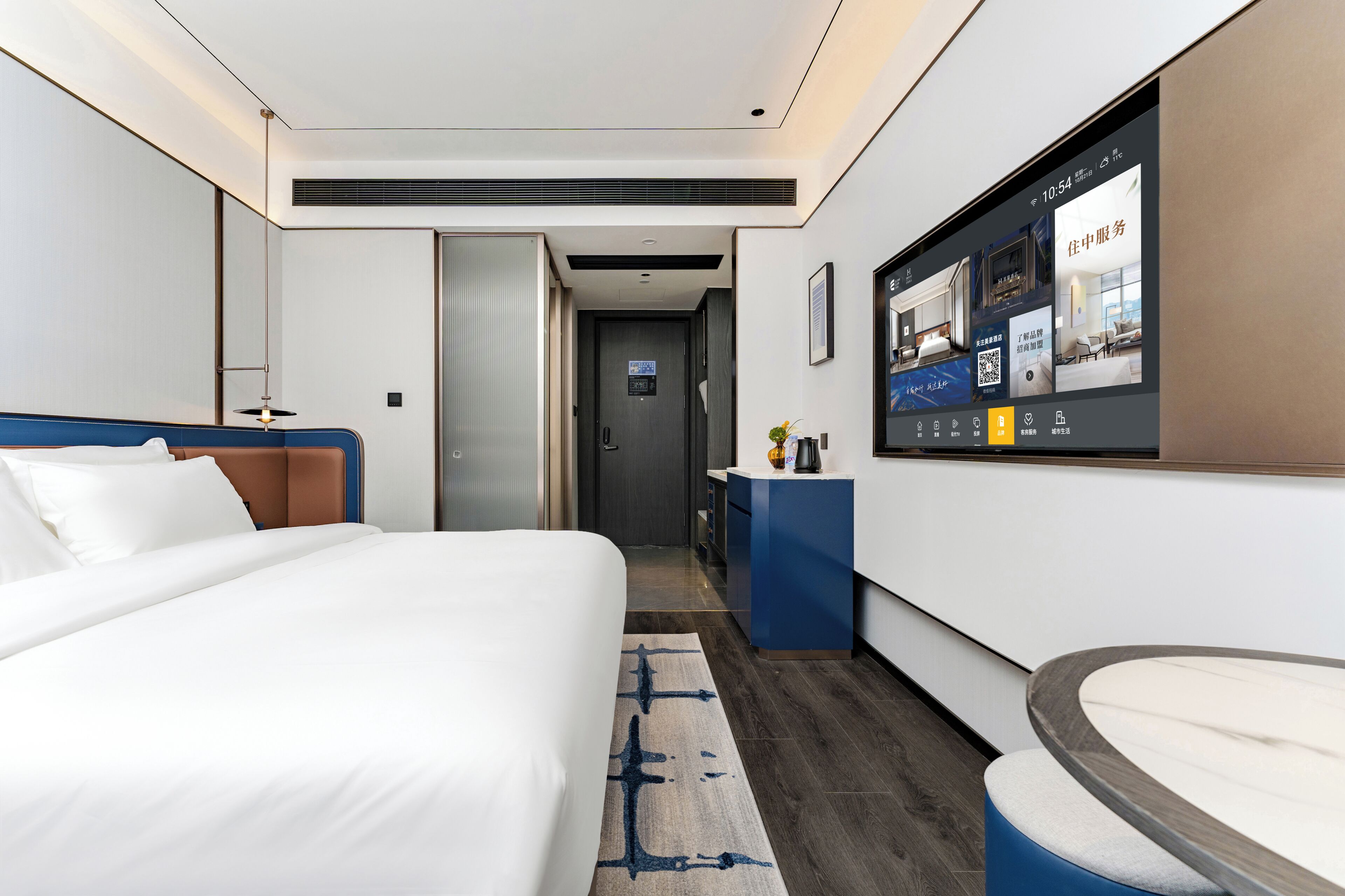Een moderne hotelkamer met een groot bed, een bureau, een televisie waarop de voorzieningen van de kamer worden getoond, en een badkamedeur.