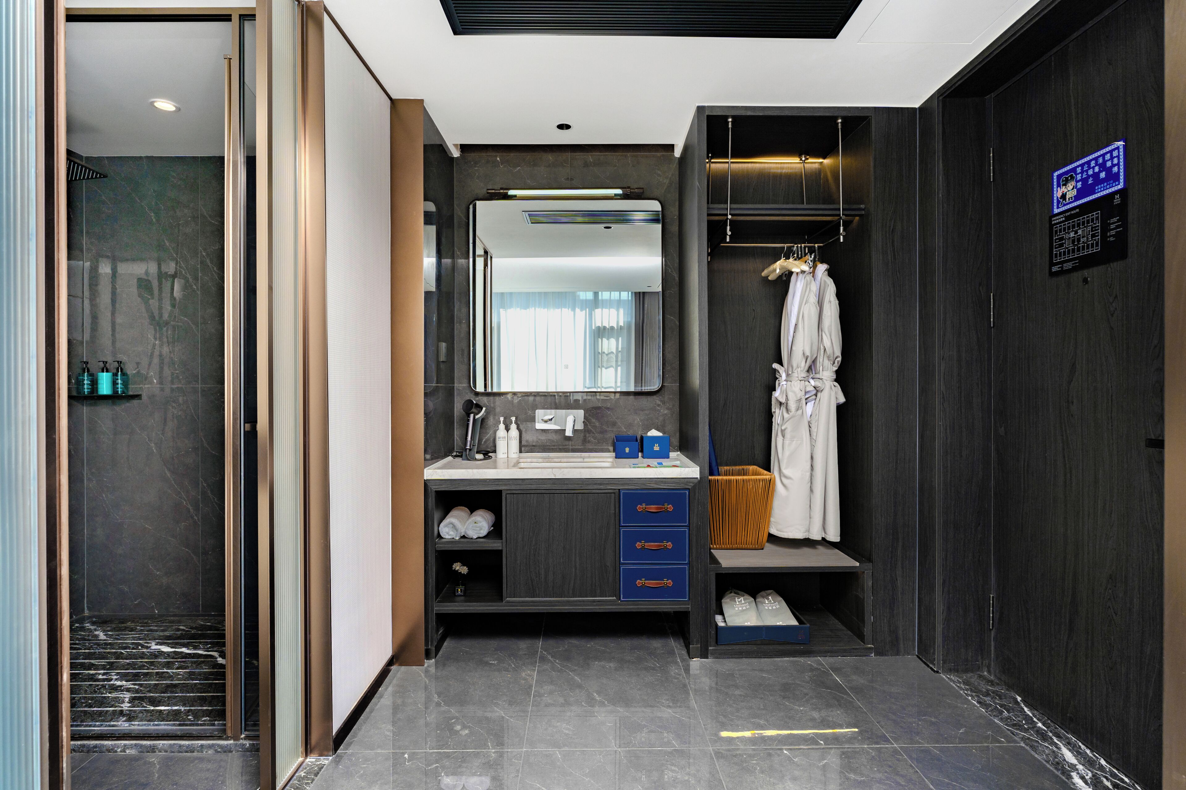 A modern bathroom with a marble floor, a large mirror, a vanity with drawers, a robe hanging, and a shower area.