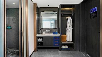 A modern bathroom with a marble floor, a large mirror, a vanity with drawers, a robe hanging, and a shower area.
